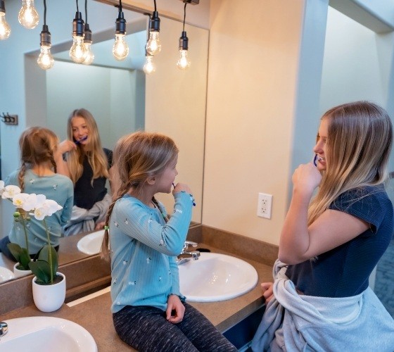 Two little girls brushing their teeth together in a bathroom