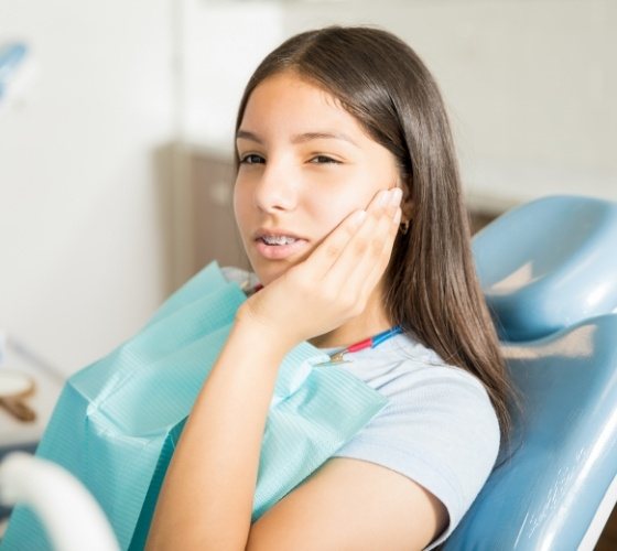 Girl in orthodontic treatment chair holding her cheek in pain