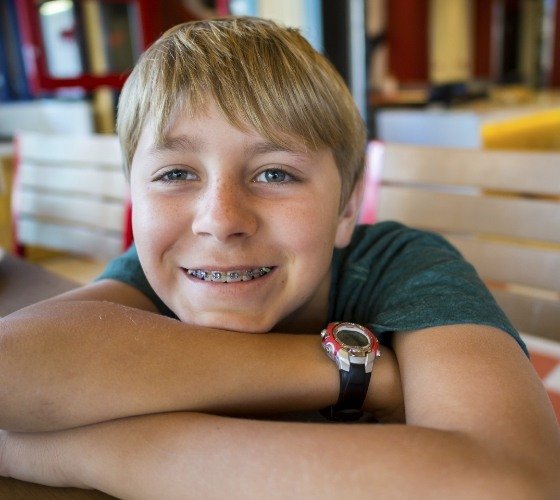 Young boy with traditional braces in Western Massachusetts sitting at table and resting his chin on his arms