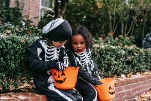 Two children in skeleton costumes looking in candy buckets