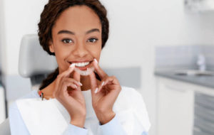 Woman in dentist’s chair inserting clear aligner